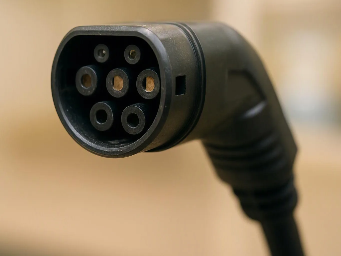 Close-up of a black electric vehicle charging plug against a soft beige background
