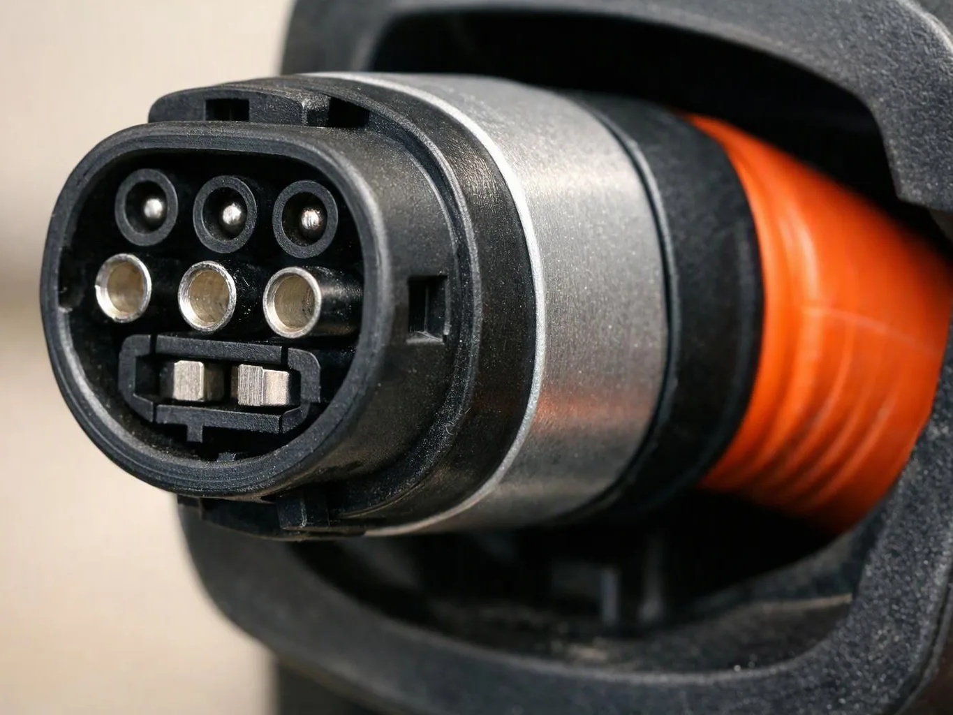 Close-up of an electric vehicle charging connector with orange cable and metal contacts against a dark background