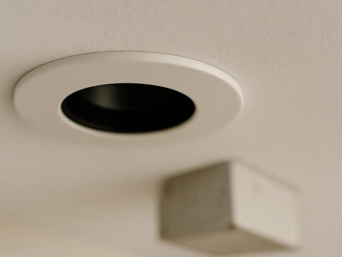 A white ceiling with a round recessed opening and a blurred rectangular fixture below it
